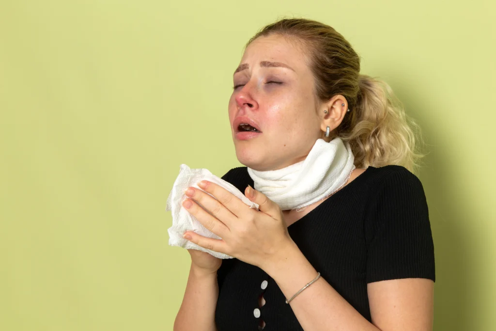 A sick woman with a bandaged neck holding a tissue to sneeze against a green background.