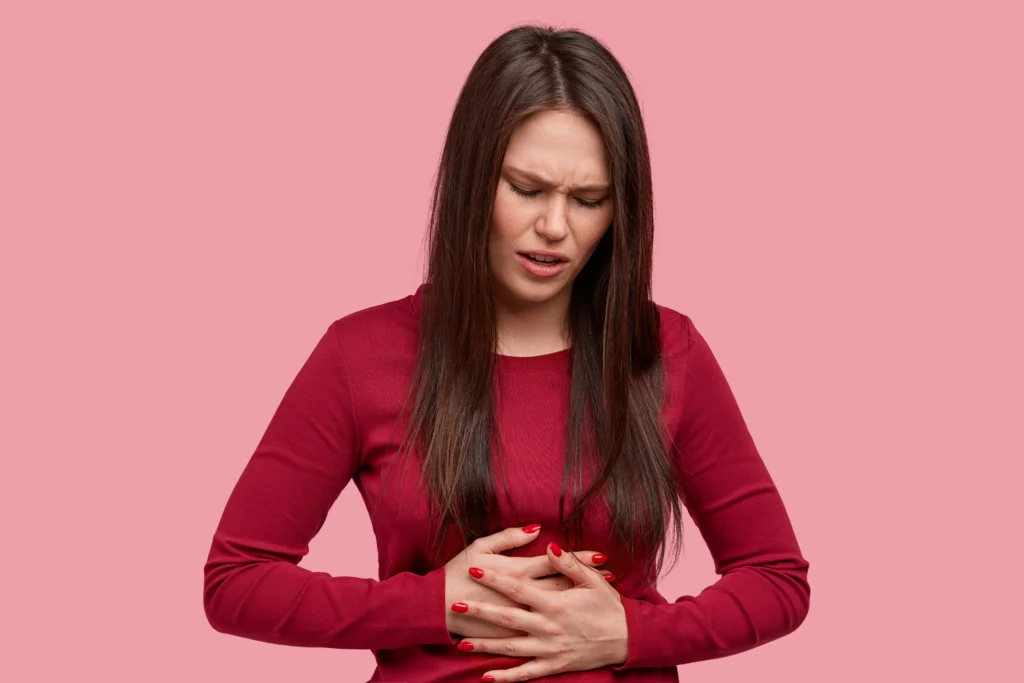 A woman holding her stomach in pain against a pink background.