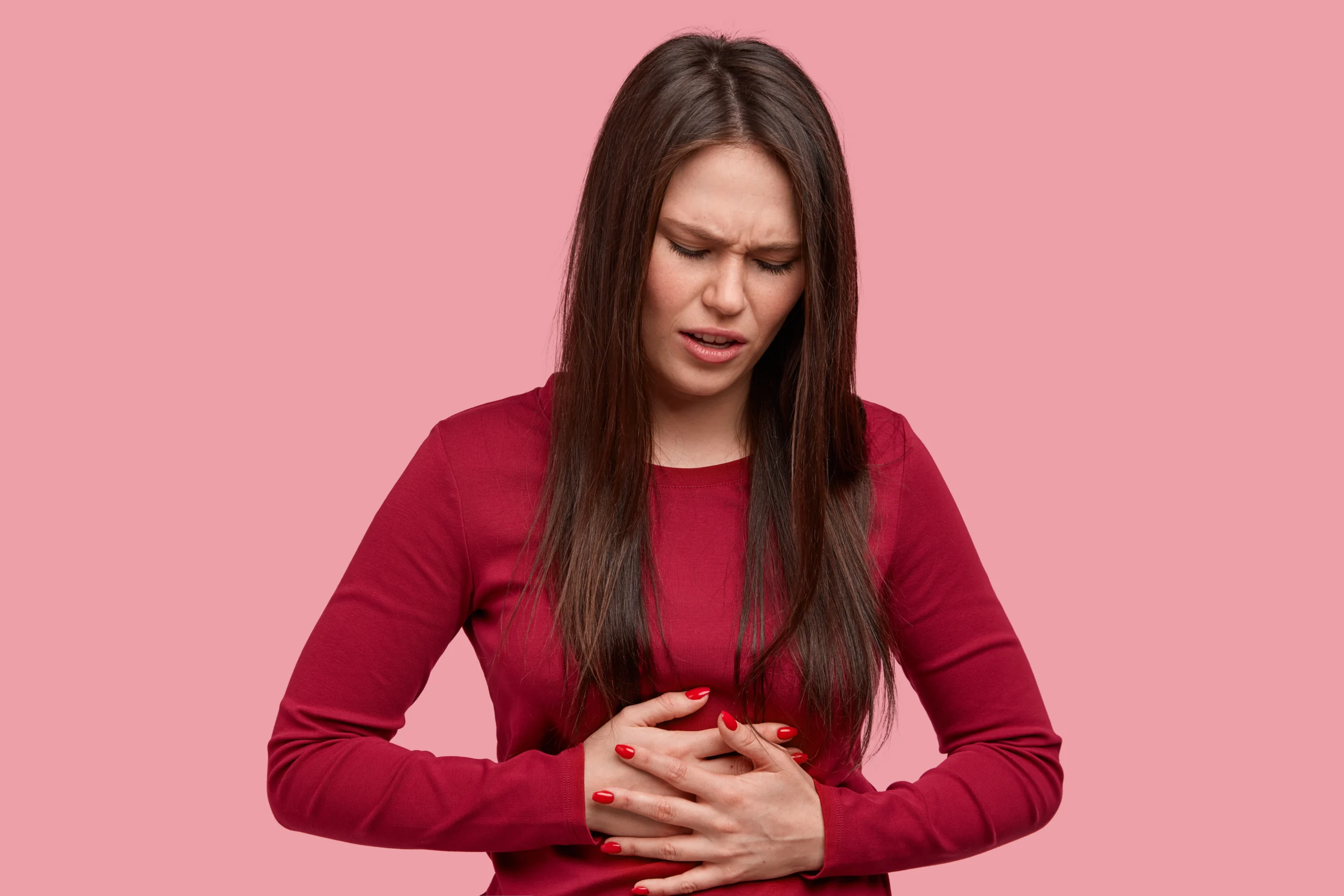 A woman holding her stomach in pain against a pink background.