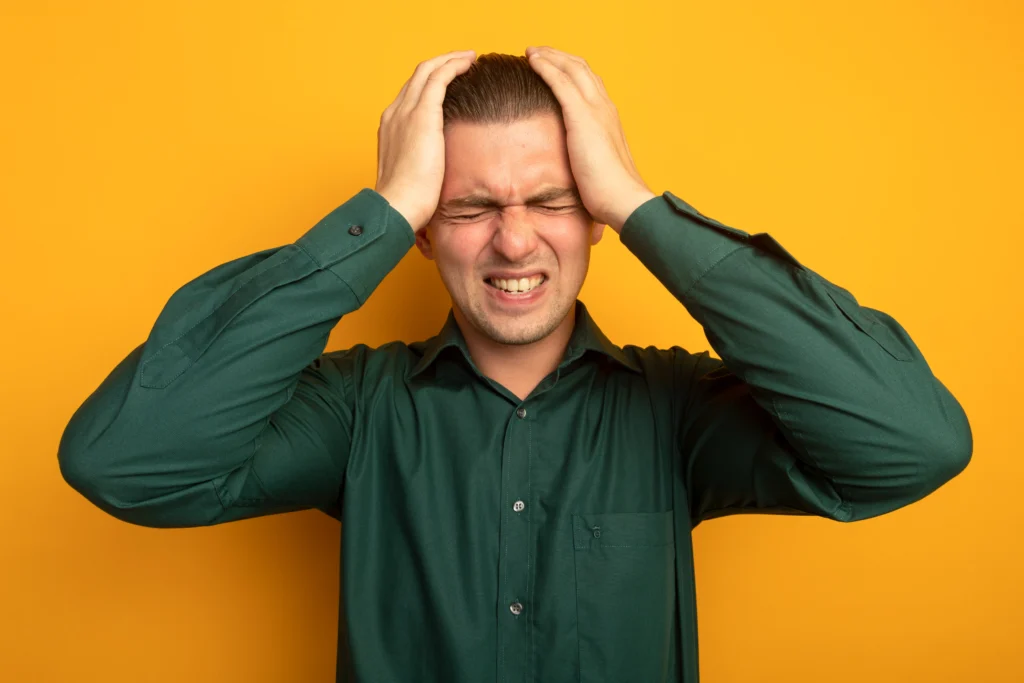 A man clutching his head and grimacing in pain against a yellow background.