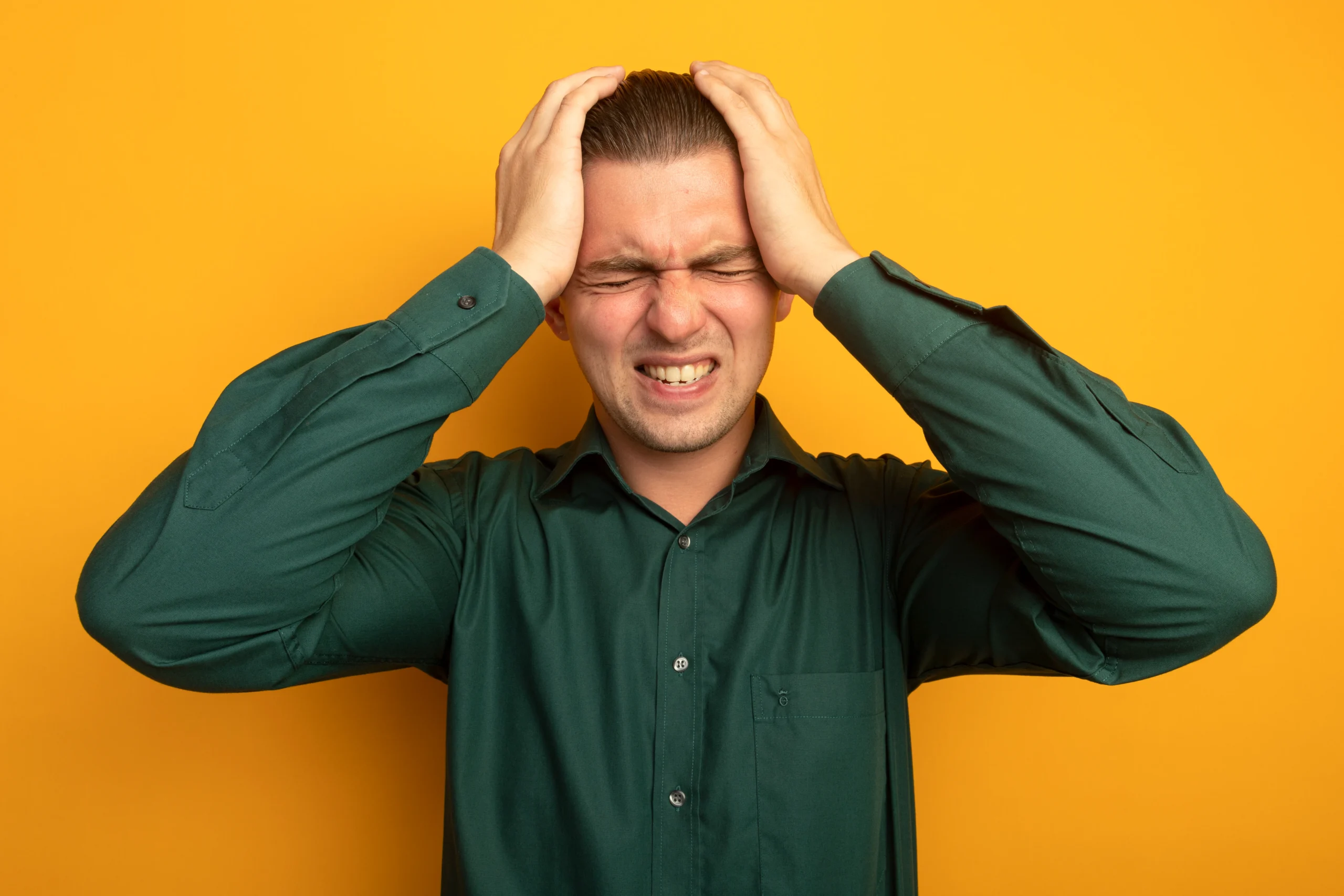A man clutching his head and grimacing in pain against a yellow background.